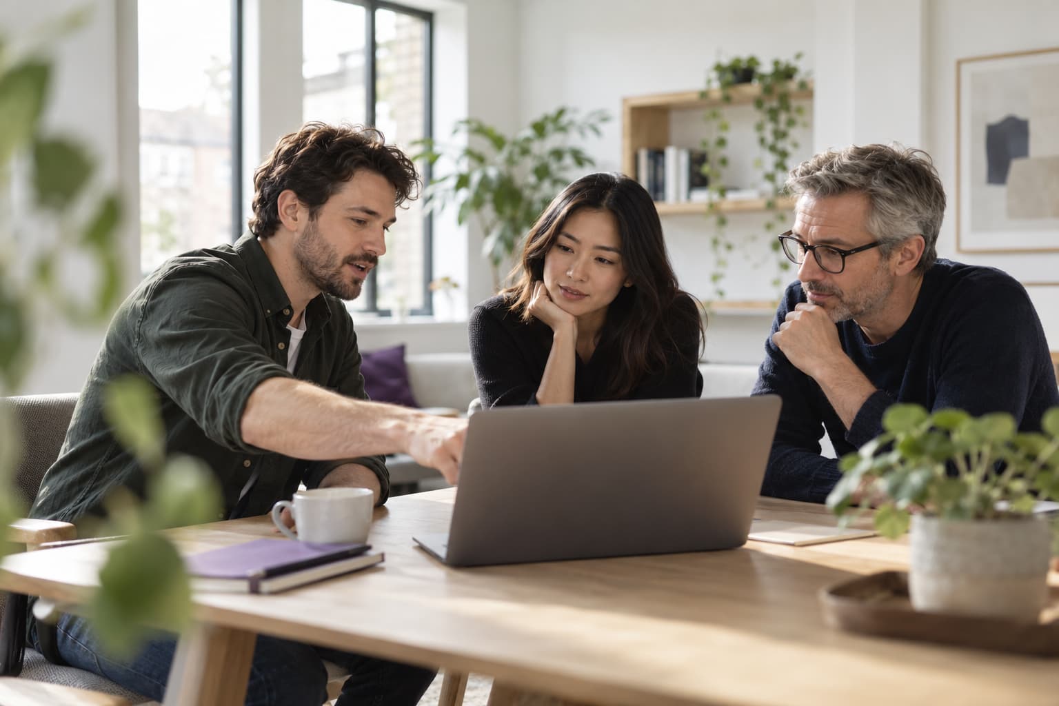 Three colleagues talking through a plan around a laptop in a bright office